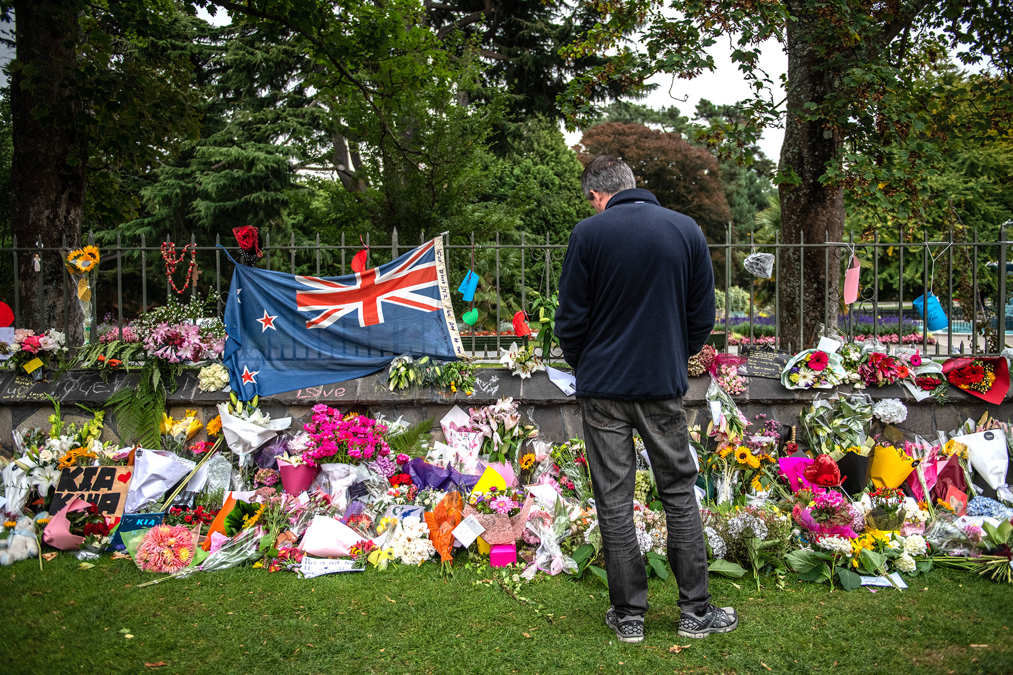PHOTO: A man pauses next to a New Zealand flag hung amongst flowers and tributes on the wall of the Botanic Gardens, March 17, 2019, in Christchurch, New Zealand for the victims of a mass shooting at two mosques. 