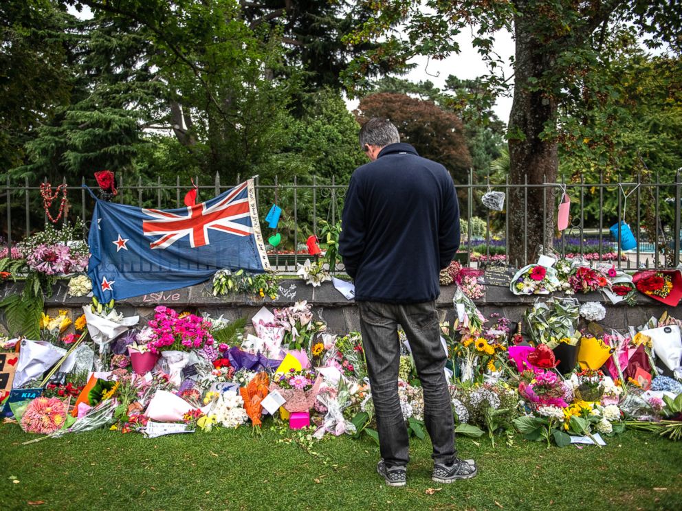 PHOTO: A man pauses next to a New Zealand flag hung amongst flowers and tributes on the wall of the Botanic Gardens, March 17, 2019, in Christchurch, New Zealand for the victims of a mass shooting at two mosques.