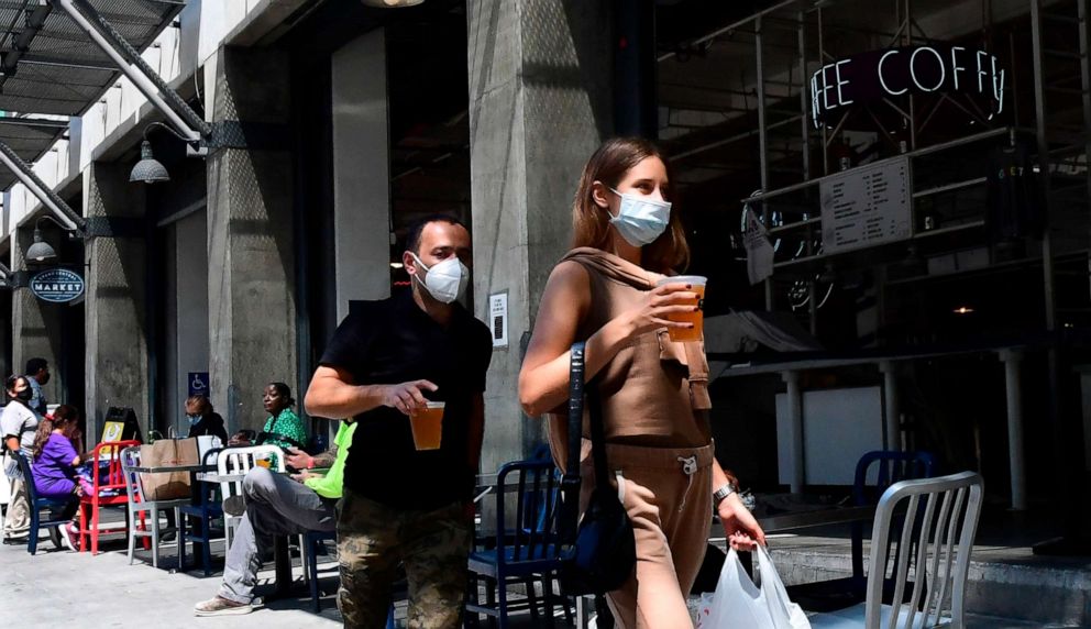 PHOTO: People wearing face masks carry their pints of beer past tables for outdoor dining in Los Angeles, California, on July 1, 2020.
