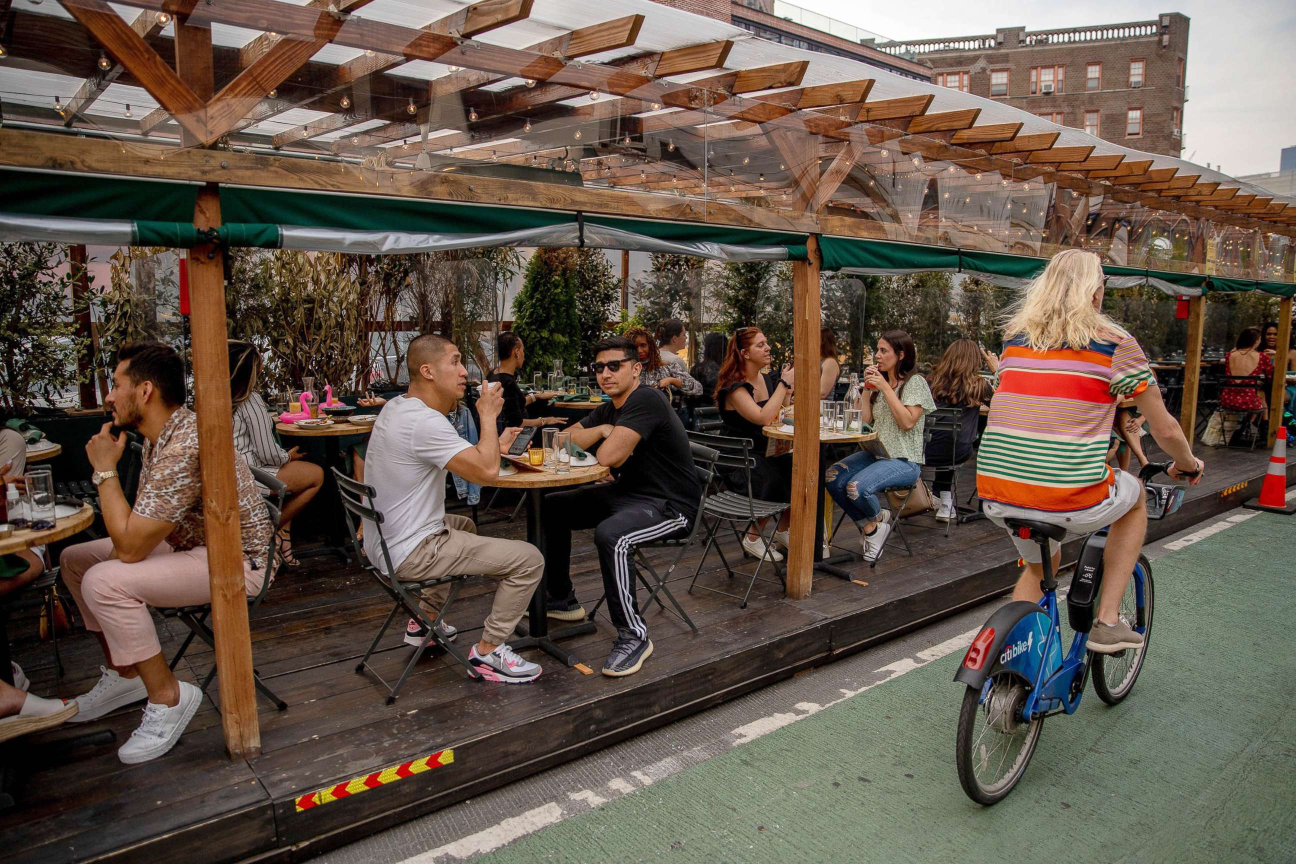 PHOTO: A person rides a bicycle past customers sitting in the outdoor dining area of a restaurant in the West Village neighborhood of New York, April 28, 2021. 