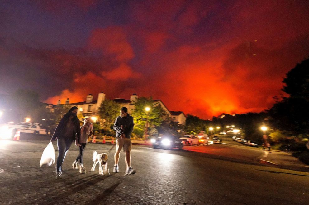 PHOTO: Residents walk a dog as a brush fire burns behind homes in the Pacific Palisades area of Los Angeles, May 15, 2021.