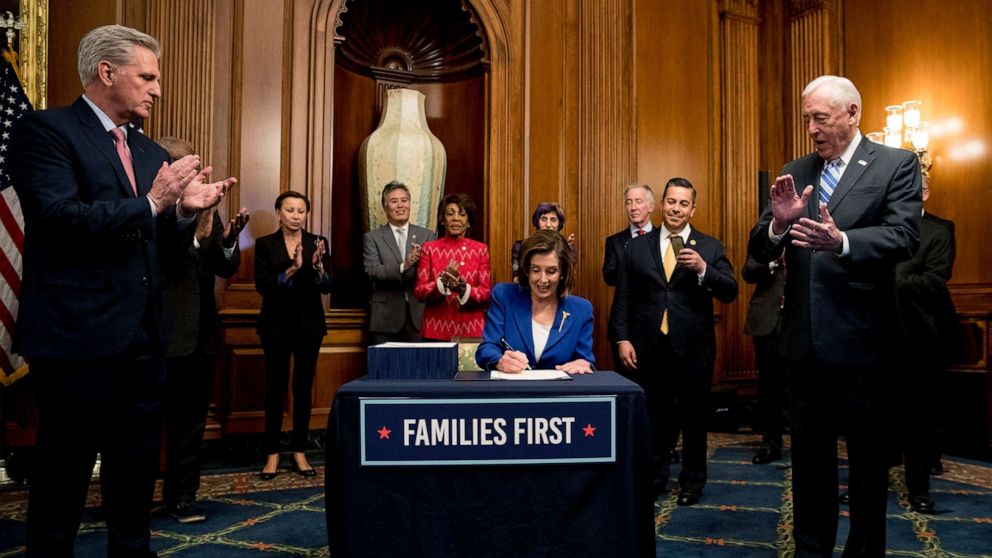 PHOTO: House Speaker Nancy Pelosi, accompanied by House Minority Leader Kevin McCarthy, left, House Majority Leader Steny Hoyer, right, and other bipartisan legislators, signs the Coronavirus Aid, Relief, and Economic Security (CARES) Act.