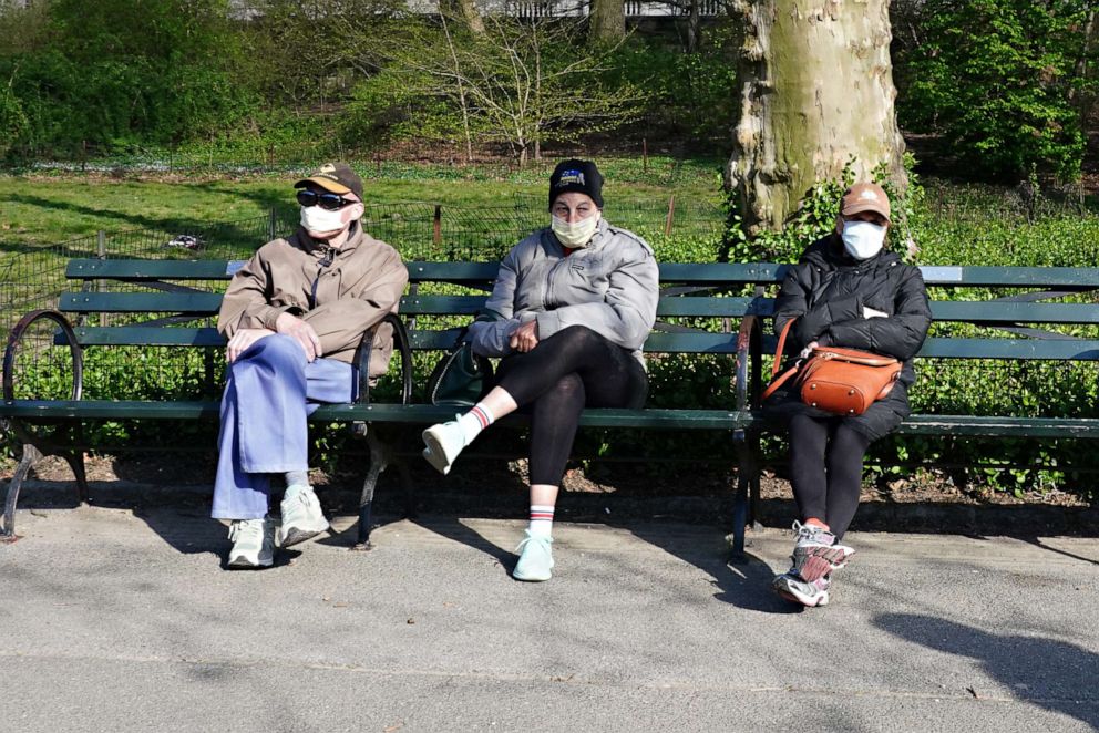 PHOTO: People wearing protective masks sit on a bench in Central Park during the coronavirus pandemic on April 11, 2020 in New York.