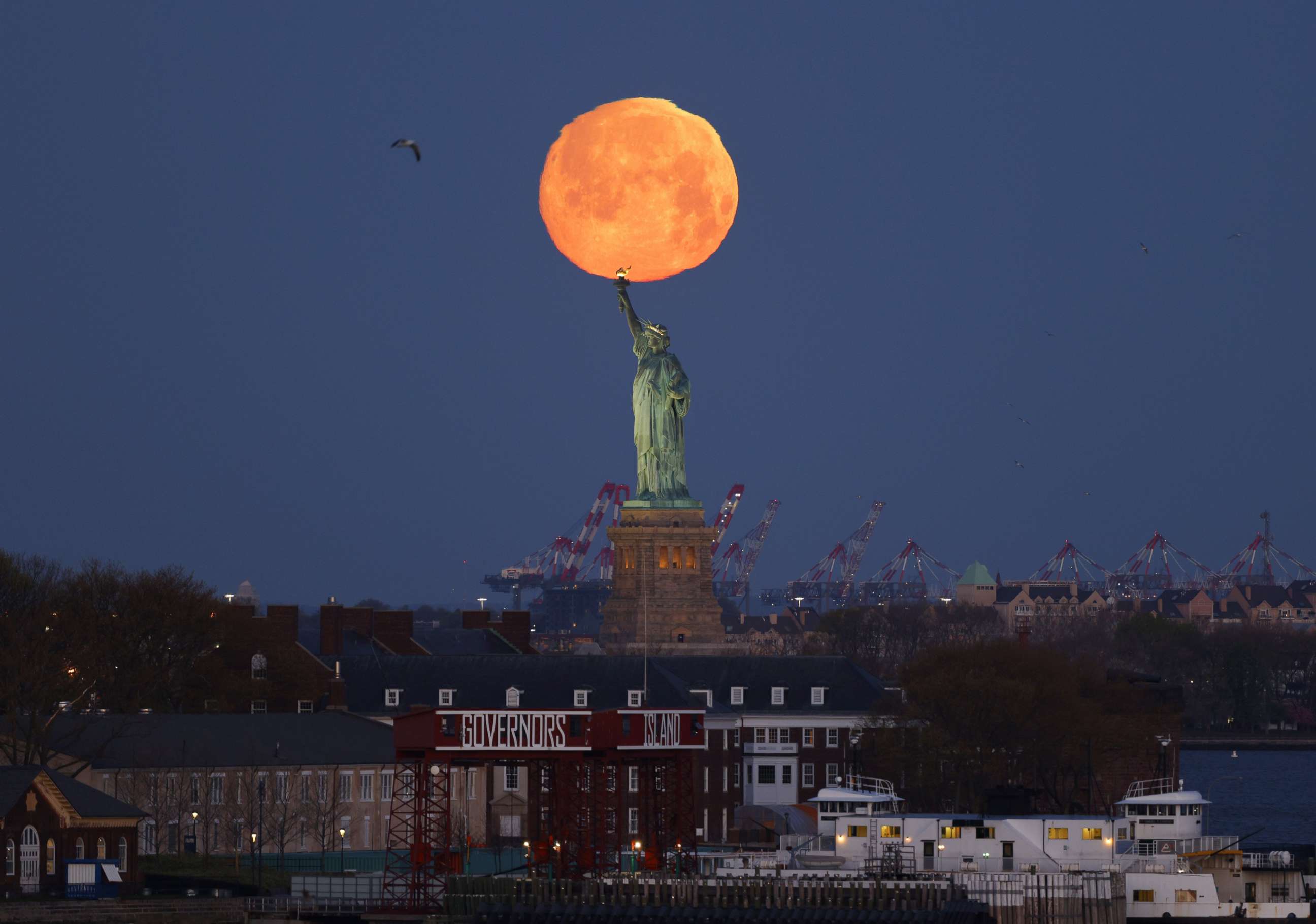 PHOTO: A Pink Supermoon sets behind the Statue of Liberty in New York, April 26, 2021.