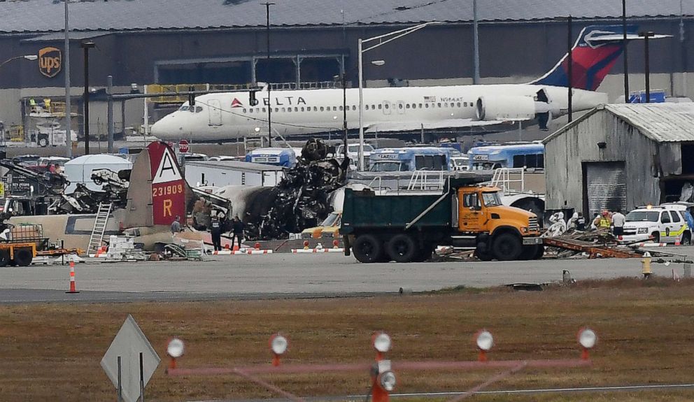 PHOTO: A Delta commercial airline plane taxis to take-off behind investigators at the wreckage of World War II-era bomber plane that crashed at Bradley International Airport in Windsor Locks, Conn., Oct. 2, 2019.