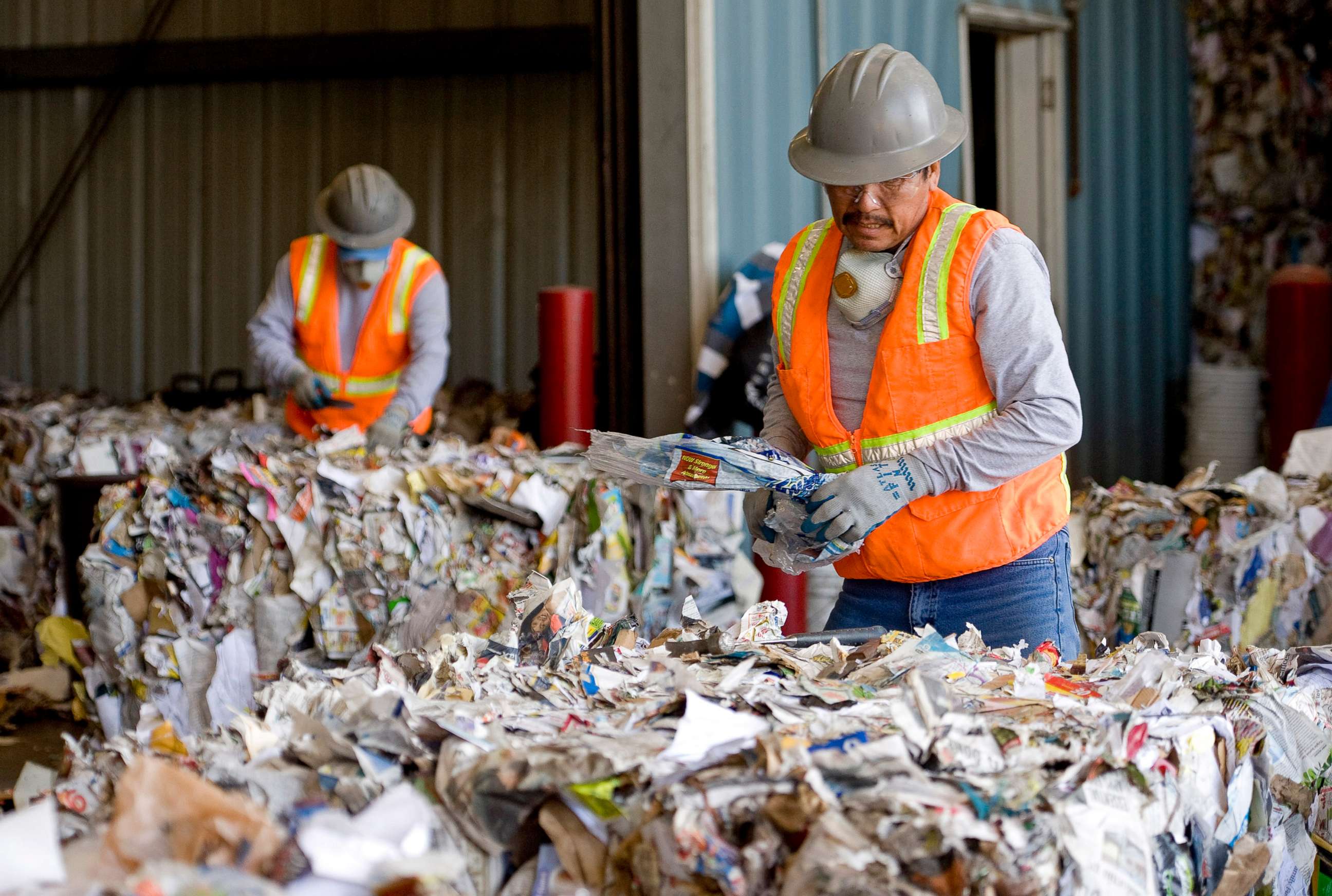 PHOTO: Workers remove plastic from piles of paper, plastic, metal and green waste at a recycling plant in Huntington Beach, Calif.