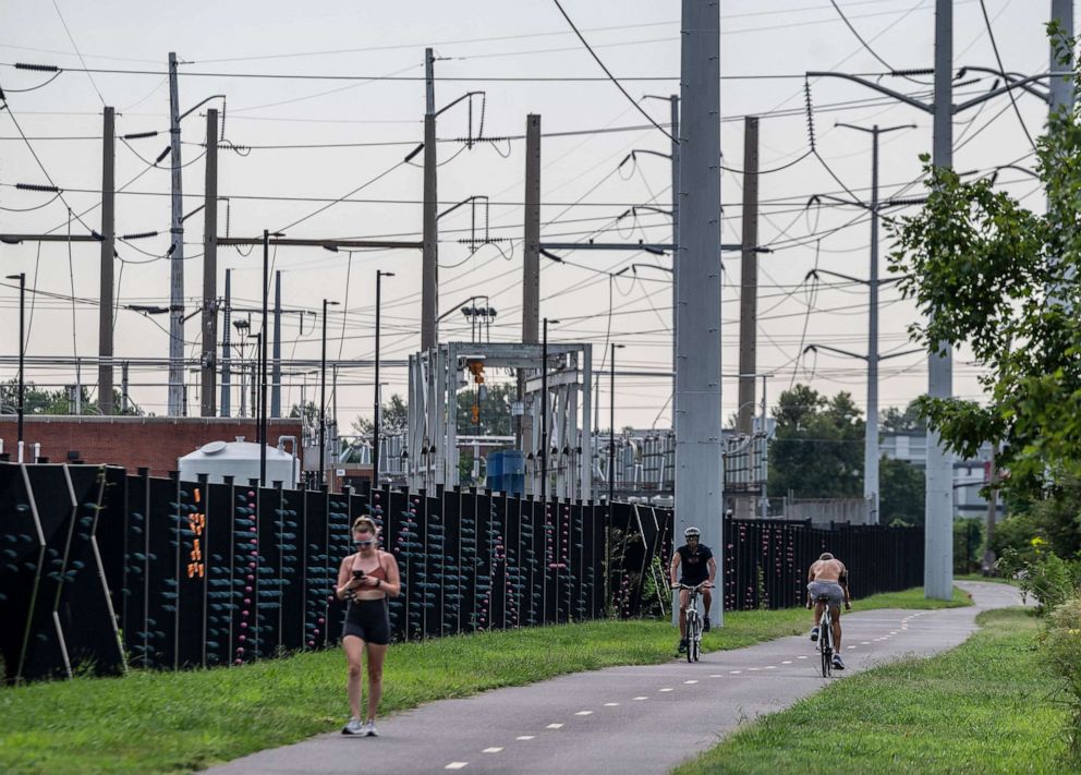 PHOTO: People pass a water treatment plant and electrical power lines on a a bike path in Arlington, Va., Aug. 13, 2021.