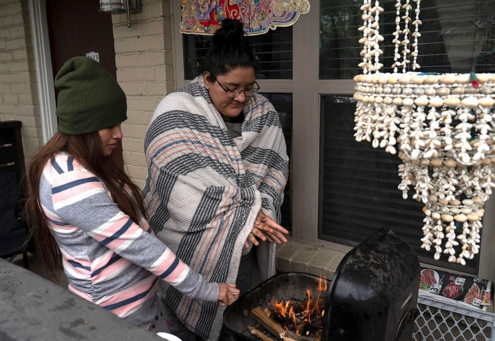 PHOTO: Karla Perez and Esperanza Gonzalez warm up by a barbecue grill during power outage caused by the winter storm on Feb. 16, 2021 in Houston. Winter storm Uri has brought historic cold weather and power outages to Texas. 