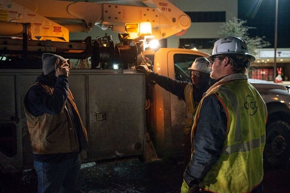 PHOTO: Oncor Electric Delivery linemen share a conversation as they wait for a new work order after repairing a utility pole damaged by snow and ice on Feb. 18, 2021, in Odessa, Texas. 