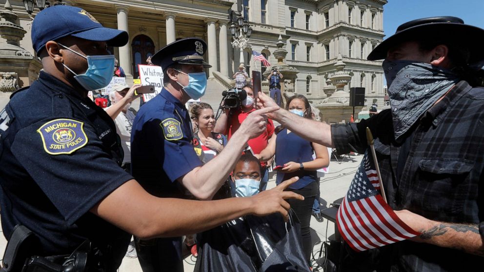 PHOTO: A person tries to help Angela Rigas as she gets a ticket for being a disorderly person as she cuts hair at the Michigan Conservative Coalition organized "Operation Haircut" outside the Michigan State Capitol in Lansing, Michigan on May 20, 2020.