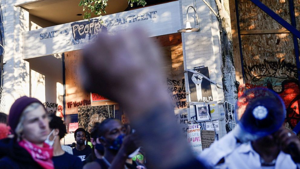 PHOTO: A protester raises a fist as others discuss strategies outside the Seattle Police Department's East Precinct within the boundaries of the so-called Capitol Hill Organized Protest zone, or CHOP, in Seattle, Washington, on June 22, 2020.