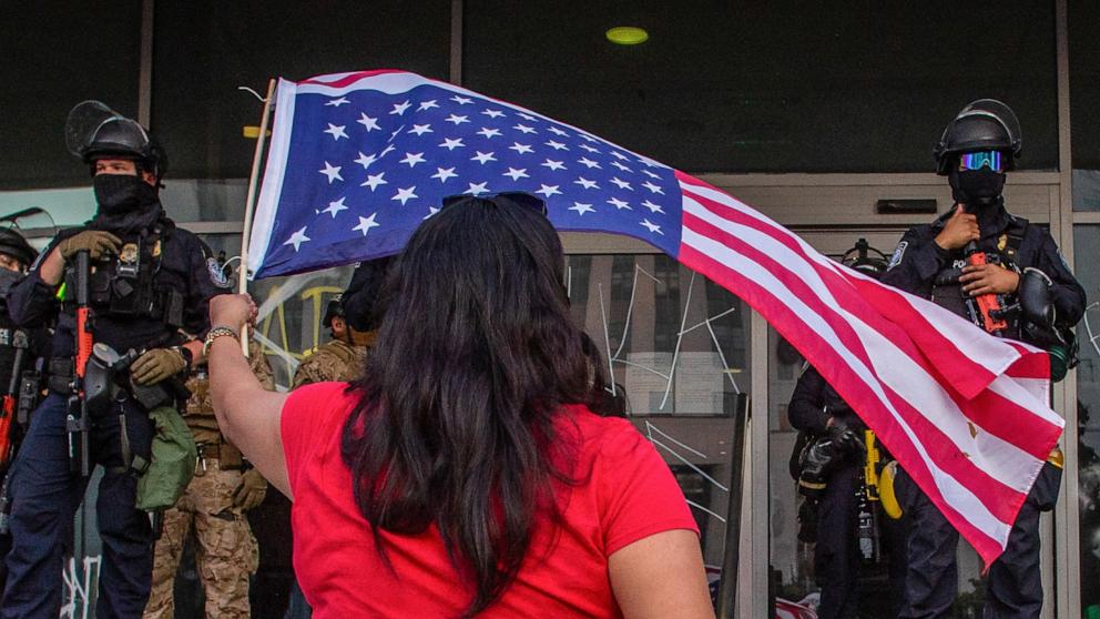 PHOTO: A woman waves a U.S. flag while California National Guard personnel stand outside the Federal Building during protests in response to federal immigration operations in Los Angeles, June 10, 2025.