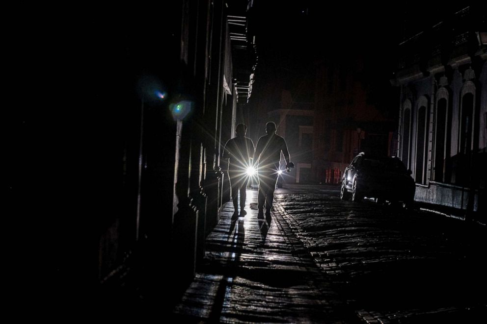 PHOTO: A cars headlights are seen past people walking on a dark in San Juan, Puerto Rico after a major power outage hit the island, April 6, 2022.