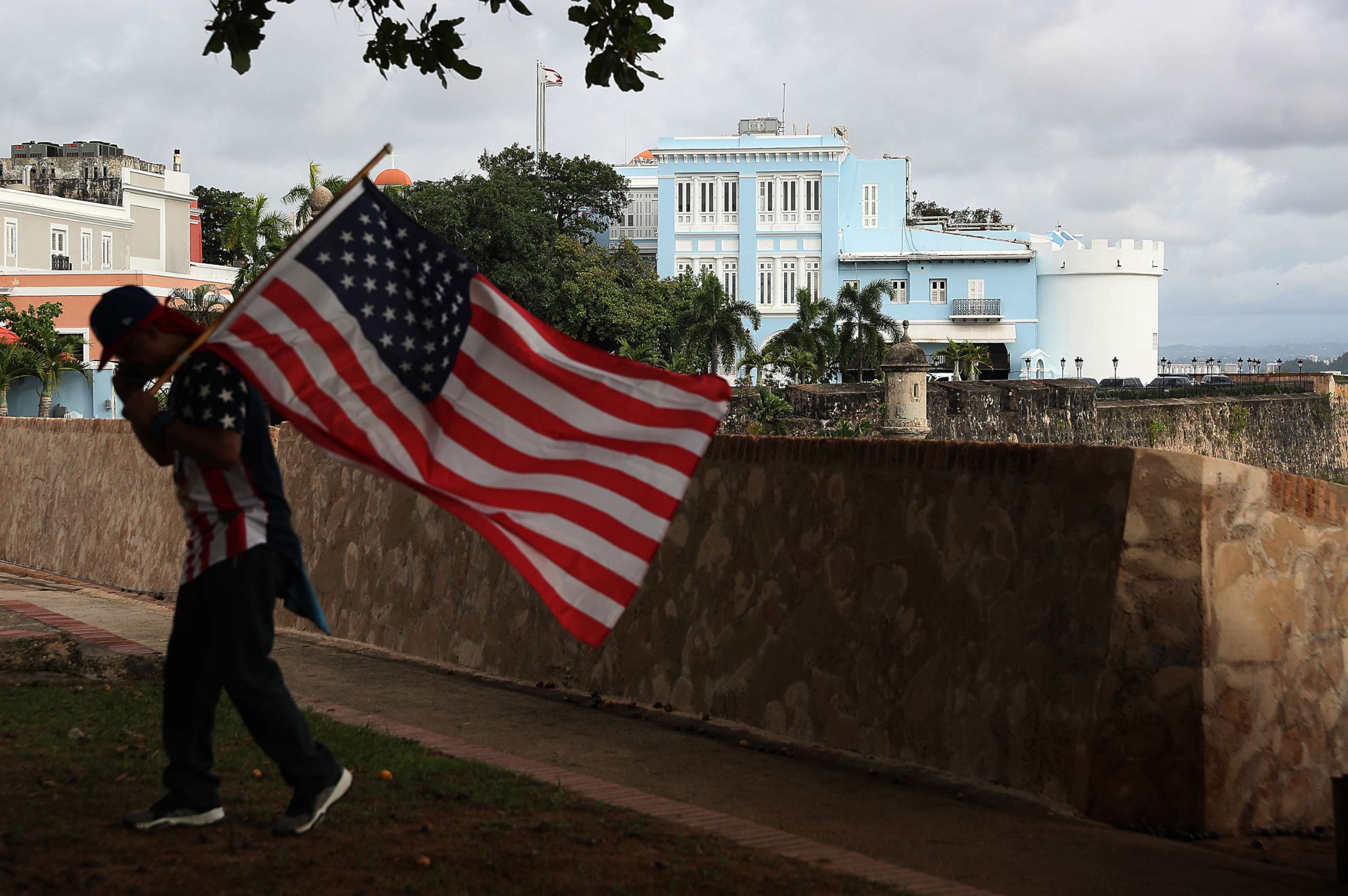 PHOTO: A man carrying a U.S. flag walks past the governor's mansion where Ricardo Rossello, the Governor of Puerto Rico lives in Old San Juan, Puerto Rico, Aug. 1, 2019.