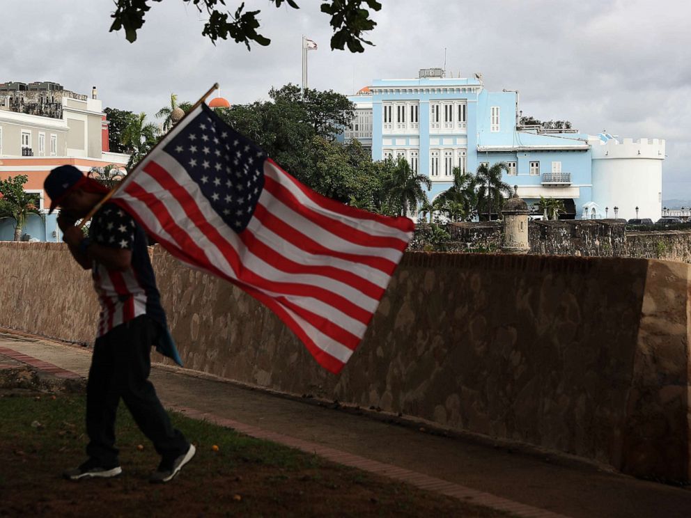 PHOTO: A man carrying a U.S. flag walks past the governors mansion where Ricardo Rossello, the Governor of Puerto Rico lives in Old San Juan, Puerto Rico, Aug. 1, 2019.