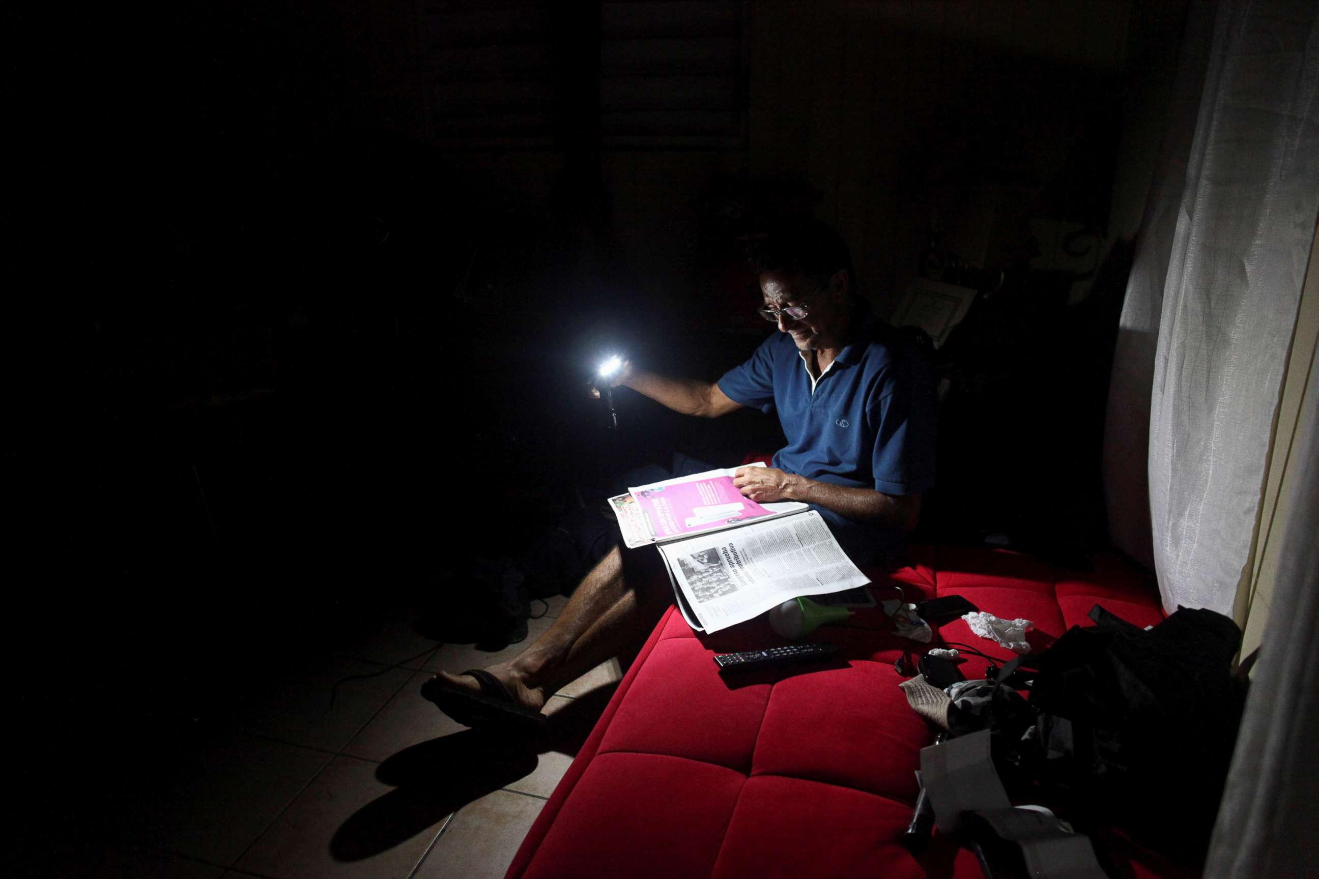 PHOTO: Hugo Regalado reads the newspaper with the help of a flashlight months after Hurricane Maria damaged the electrical grid in Dorado, Puerto Rico, Jan. 15, 2018.