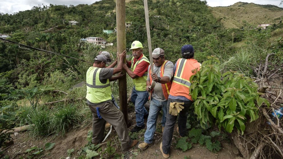 Public Works Sub-Director Ramon Mendez, wearing hard hat, directs locals who are municipal workers, Eliezer Nazario, holding rope, Tomas Martinez, right, and Angel Diaz, left, as they install a power pole in an effort to return electricity to Felipe Rodriguez's home, four months after Hurricane Maria in Coamo, Puerto Rico, Jan. 31, 2018.