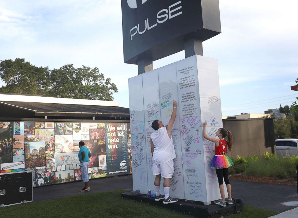 PHOTO: Jim McDermott (L) and Isabella Andriolo, 11, write messages on the Pulse sign as they visit the memorial to the 49 shooting victims setup at the Pulse nightclub where the shootings took place two years ago, June 12, 2018, in Orlando, Fla.