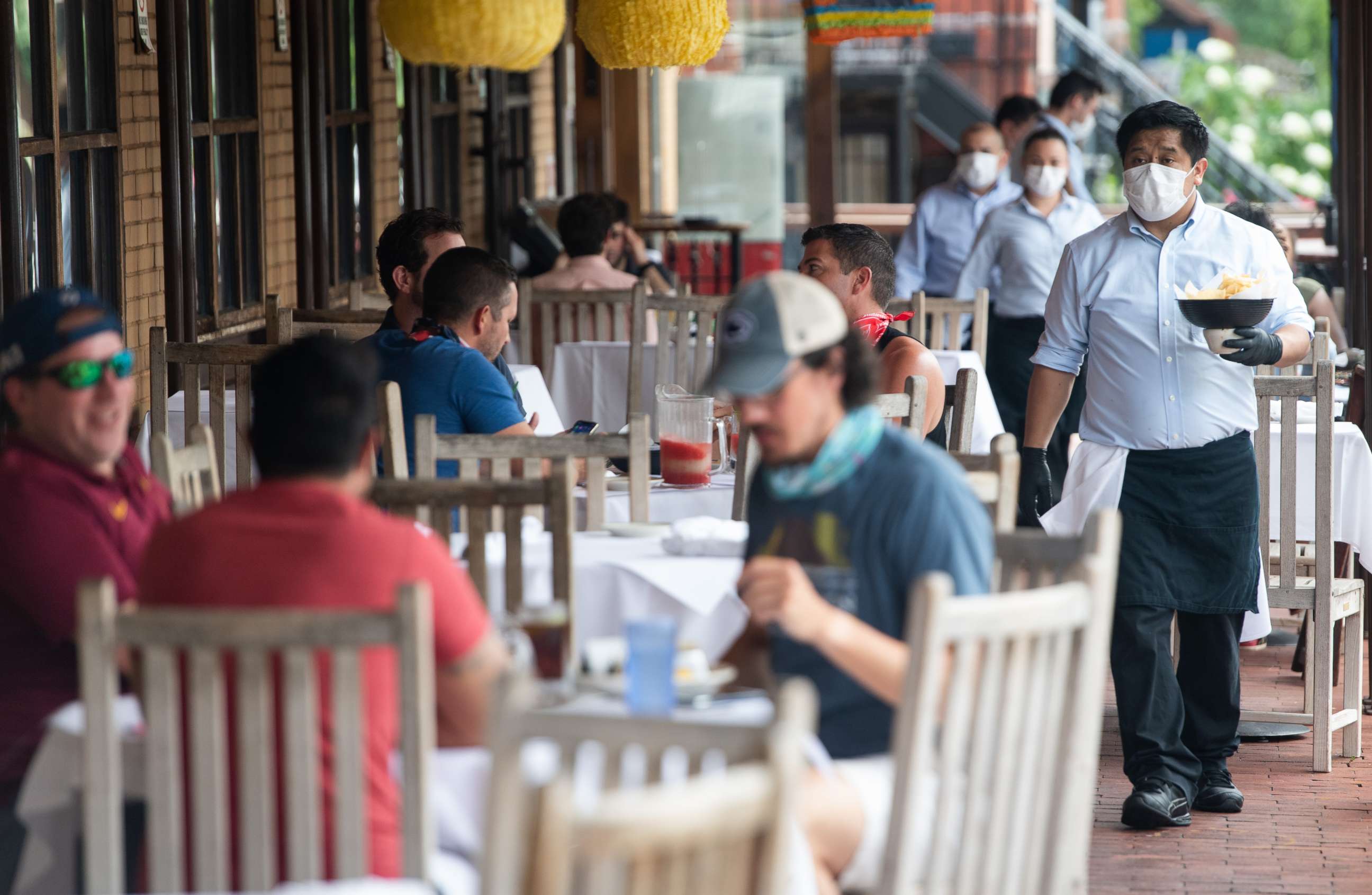 PHOTO: A waiter wearing a mask and gloves delivers food to a table to customers seated at an outdoor patio at a Mexican restaurant in Washington, May 29, 2020.