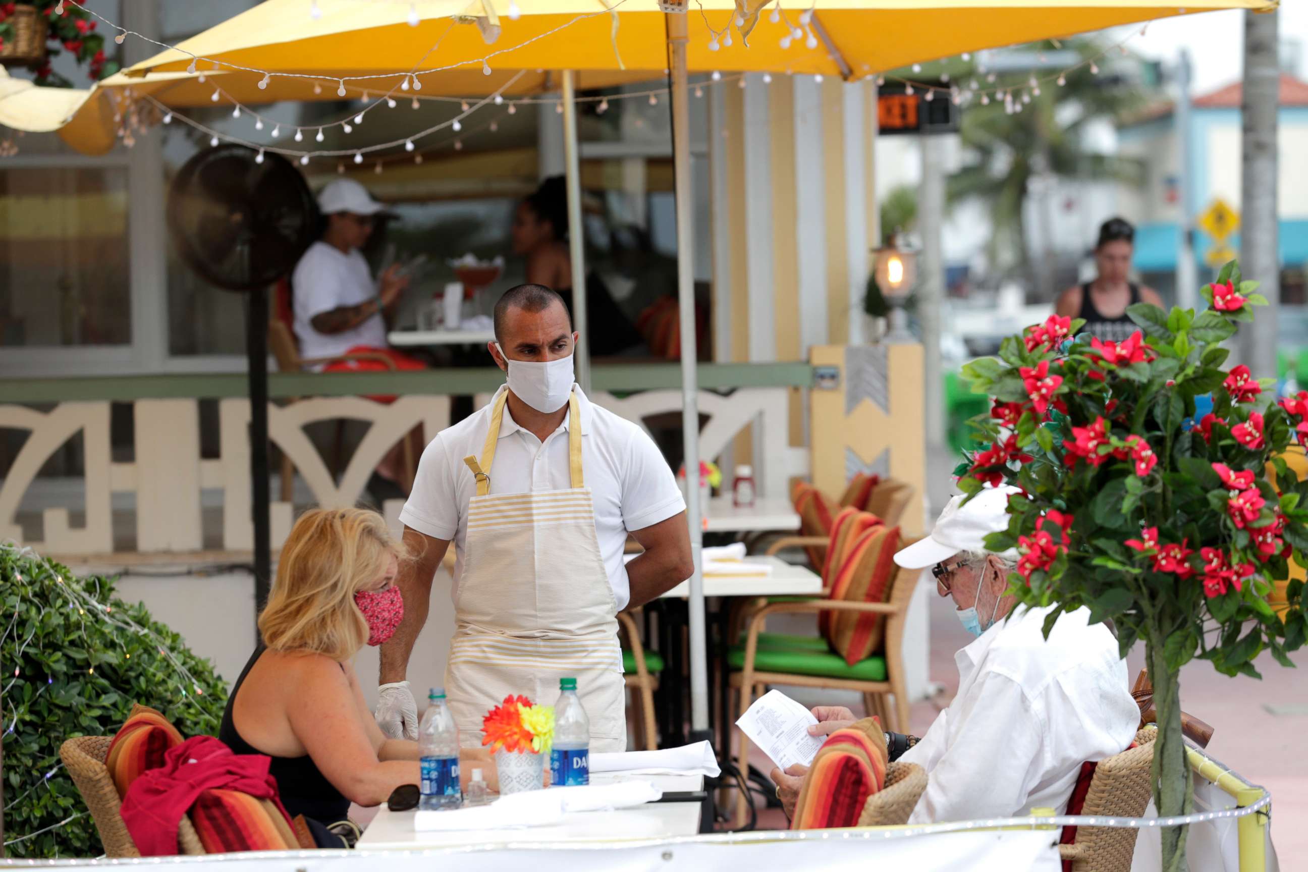 PHOTO: Jeffrey Holinka wears a protective face mask as he waits to receive an order at the On Ocean 7 Cafe along Ocean Drive in Miami Beach, Fla. during the new coronavirus pandemic, May 27, 2020. 