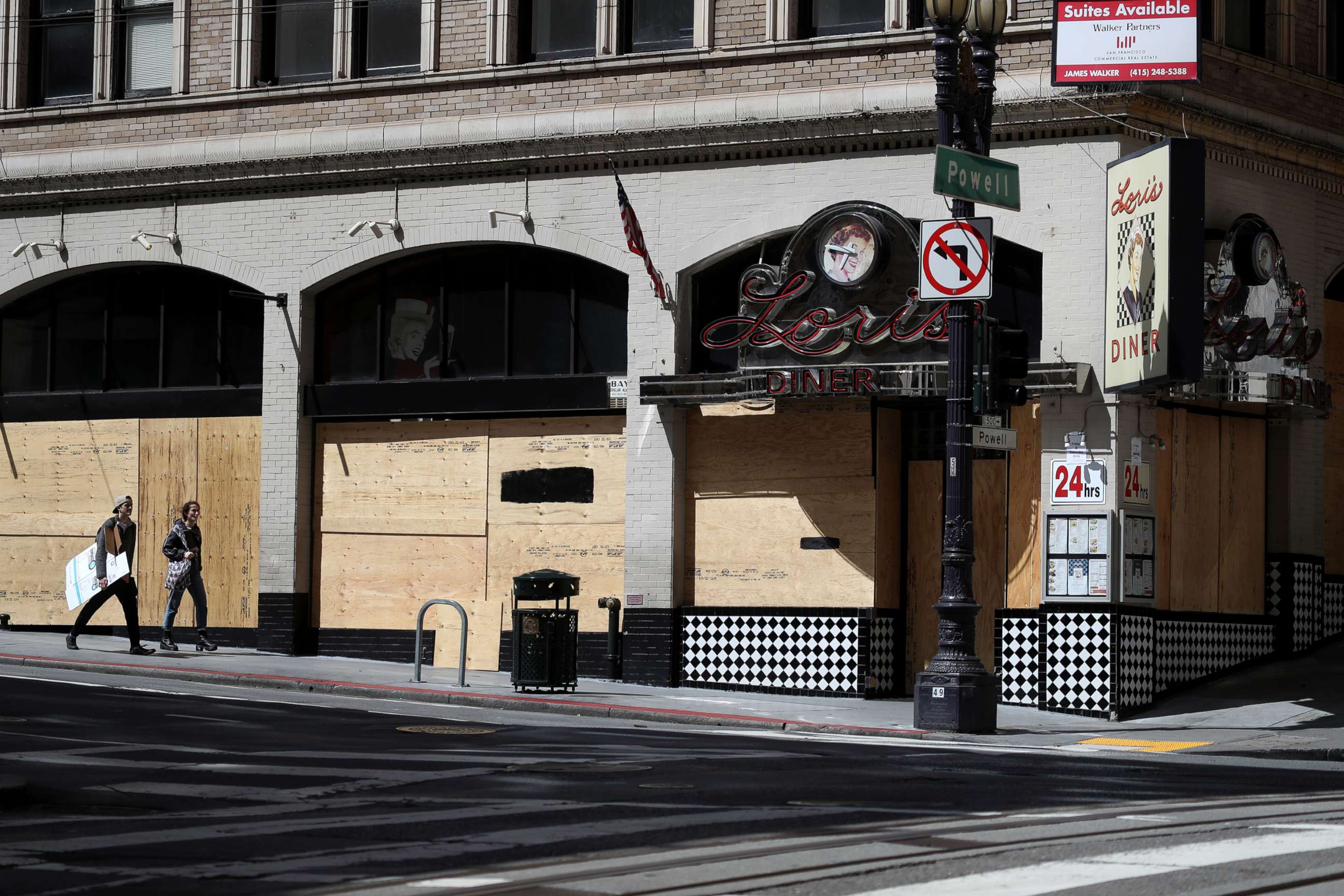 PHOTO: Pedestrians walk by a boarded up restaurant, March 31, 2020, in San Francisco, Calif.
