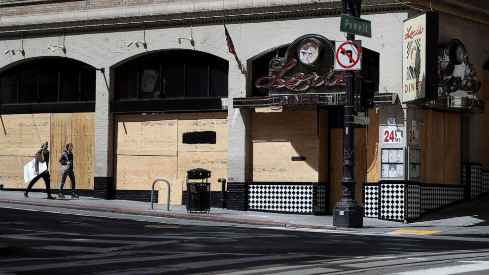 PHOTO: Pedestrians walk by a boarded up restaurant, March 31, 2020, in San Francisco, Calif.