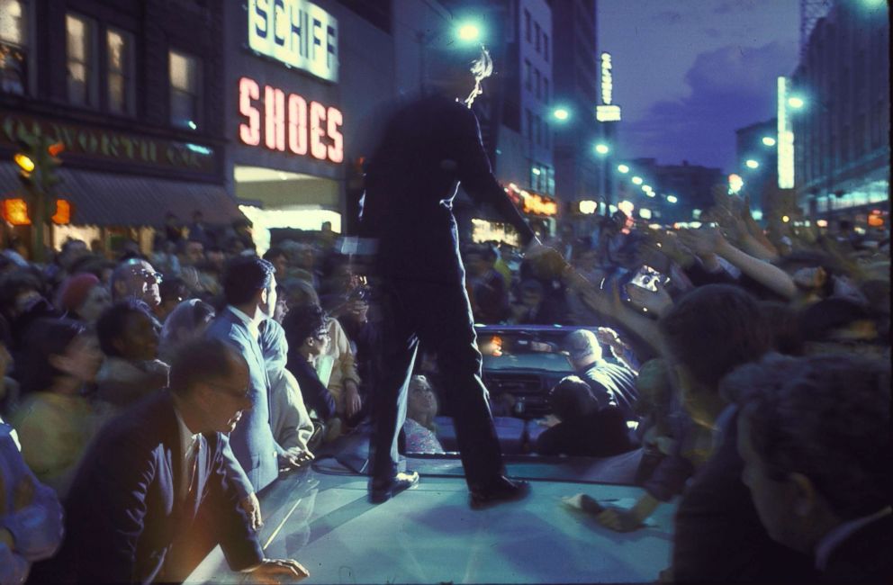 PHOTO: Presidential candidate Robert Kennedy, standing on back of convertible car while campaigning during evening hours, 1968.