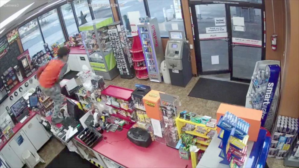 PHOTO: 2 young males appear to step around collapsed clerk to rob store.