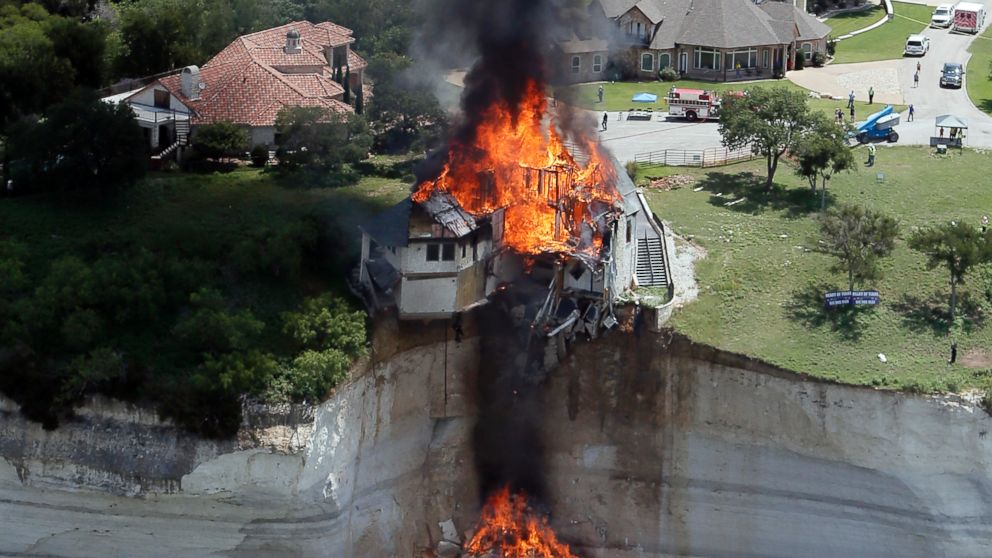 Smoke rises from a house deliberately set on fire, days after part of the ground it was resting on collapsed into Lake Whitney, Texas, June 13, 2014. Building crews set fire to the luxury lake house left dangling about 75 feet on a decaying cliff.