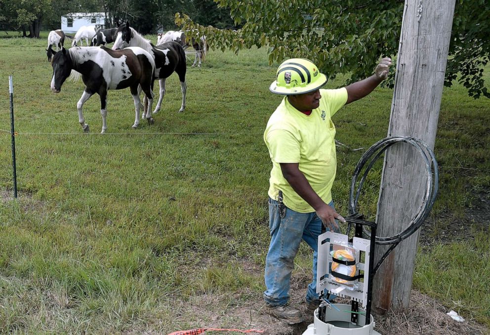 PHOTO: Horses gaze in a field as a utility worker helps install equipment for high speed internet cable in the rural Pocahontas area in Northern Coffee County, Tenn., on Aug. 22, 2018.