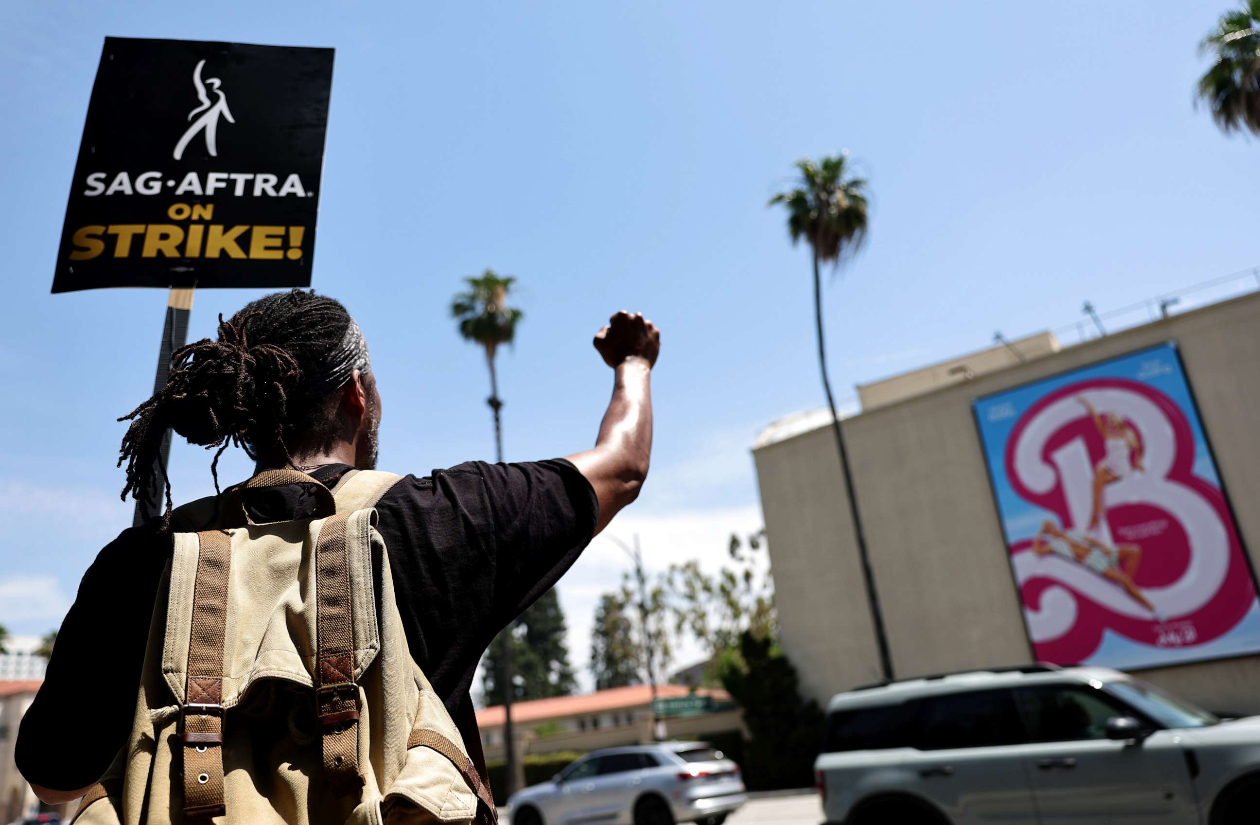PHOTO: Striking SAG-AFTRA member James Mathis III pickets with other SAG-AFTRA members and striking WGA (Writers Guild of America) workers outside Warner Bros. Studio, near a billboard for the Barbie movie, on July 17, 2023 in Burbank, California.
