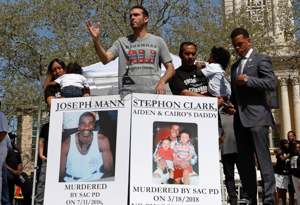 PHOTO: Salena Manni (L), fiancee of Stephon Clark, holds their son Cairo and an unidentified man holds son Aiden (2nd R) while Basim Elkarra speaks and Rev. Shane Harris listens at a rally in Sacramento, Calif., March 31, 2018.