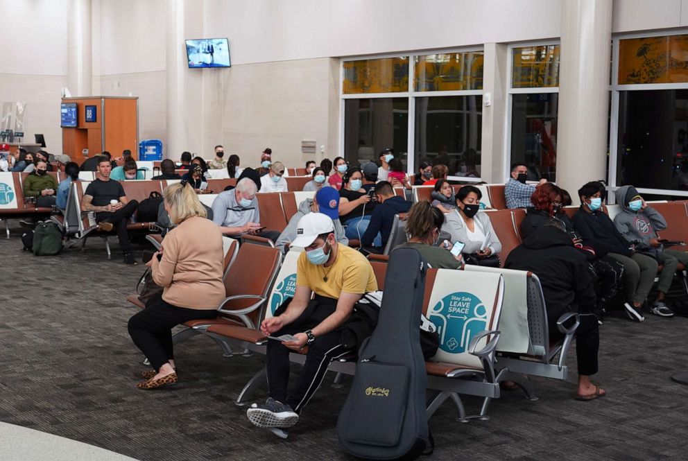 PHOTO: People with face masks sit between physical and social distancing marker signs with the words "Stay Safe. Leave Space" on seats in Terminal B of the San Antonio International Airport, March 31, 2021, in San Antonio, Texas.