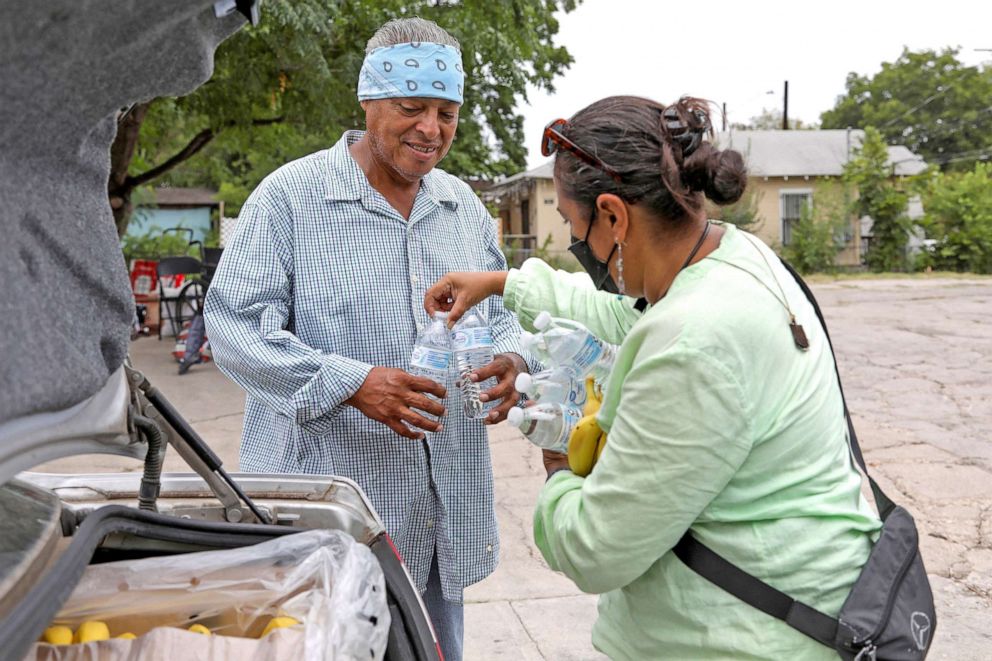 PHOTO: Susana Segura, with Bread and Blankets Mutual Aid, gives out water, bananas and hats to ward off the sun to unhoused people and others in need during a heat advisory in San Antonio, July 21, 2022.  