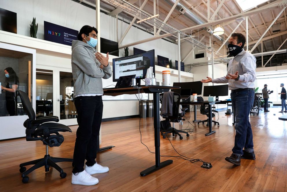PHOTO: In this March 24, 2021, file photo, tech startup company Fast Chief Communications Officer Jason Alderman (R) talks with an employee on the first day working in the office in San Francisco.