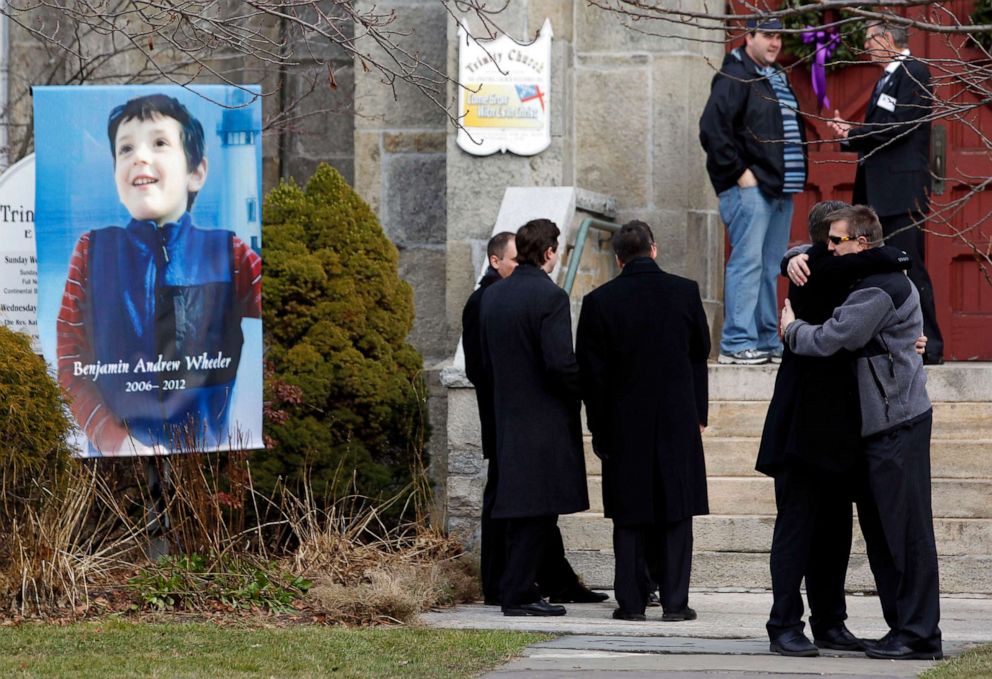 PHOTO: Mourners embrace outside of Trinity Episcopal Church while standing next to a portrait of Benjamin Andrew Wheeler, one of the students killed in the Sandy Hook Elementary School shooting, Dec. 20, 2012, in Newtown, Conn.