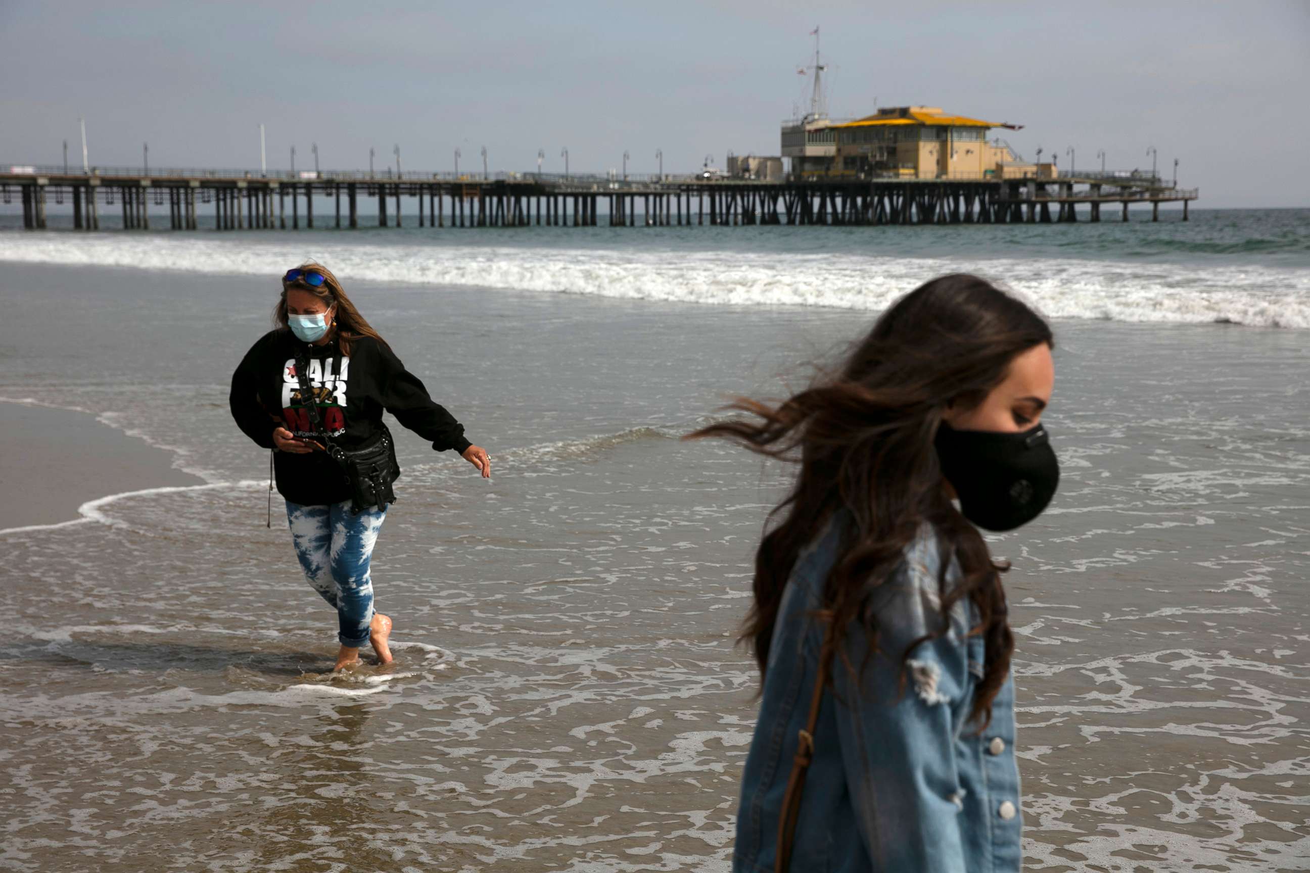 PHOTO: Malia Pena, foreground, and her mother, Lisa Torriente, wear masks as they visit the beach, June 23, 2020, in Santa Monica, Calif.
