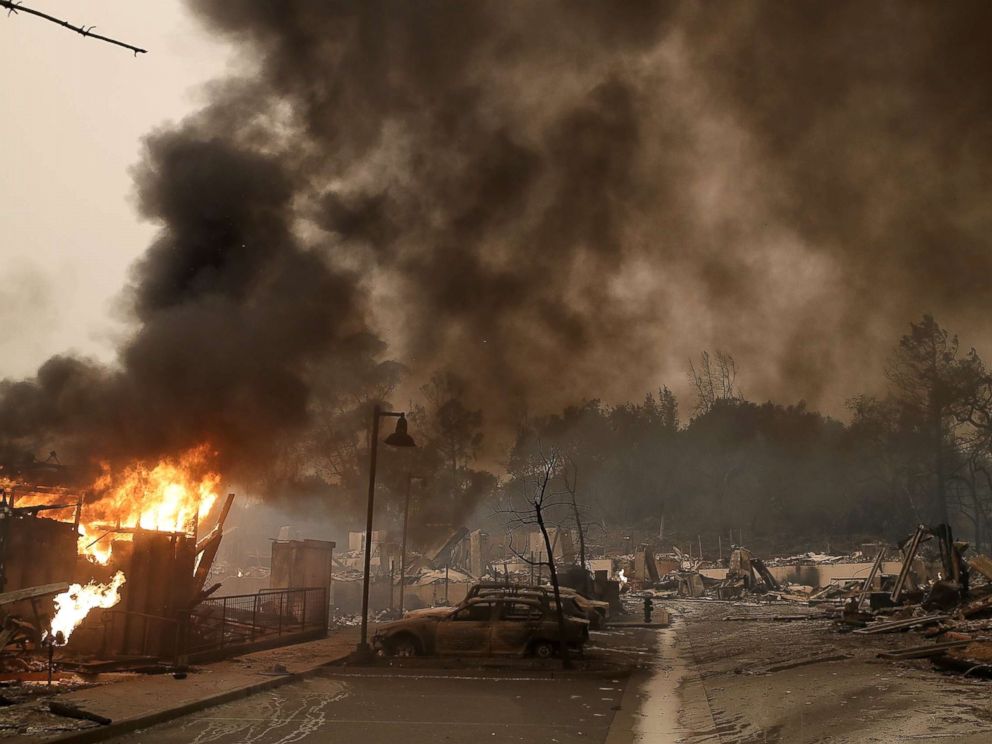 PHOTO: Burned out cars sit next to a building on fire in a fire ravaged neighborhood on Oct. 9, 2017 in Santa Rosa, Calif.