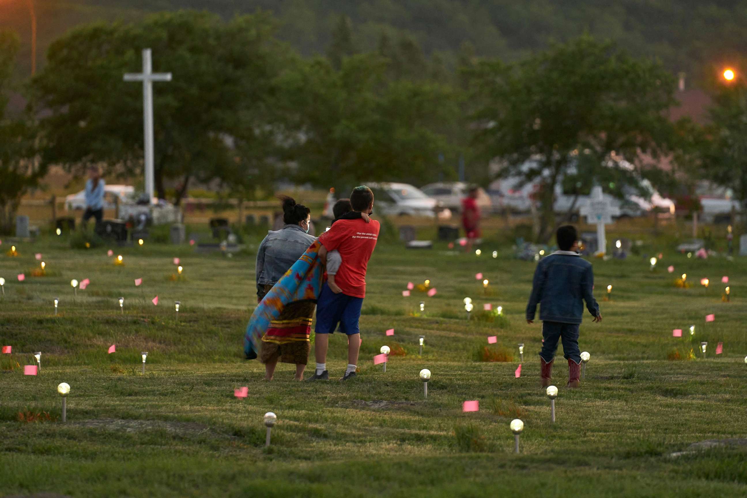 PHOTO: A family walks through a field where flags and solar lights now mark the site where human remains were discovered in unmarked graves at the former Marieval Indian Residential School site on Cowessess First Nation, Saskatchewan, June 26, 2021. 