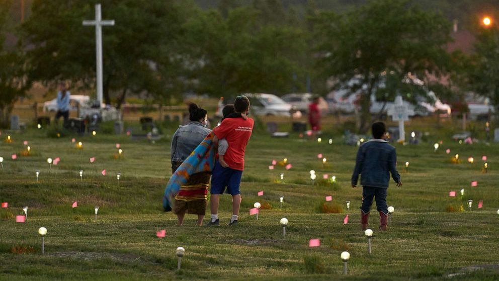 PHOTO: A family walks through a field where flags and solar lights now mark the site where human remains were discovered in unmarked graves at the former Marieval Indian Residential School site on Cowessess First Nation, Saskatchewan, June 26, 2021.