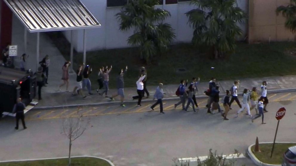 PHOTO: People emerge from a building with their hands raised after reports of a shooting at Stoneman Douglas High School in Parkland, Fla., Feb. 14, 2018.
