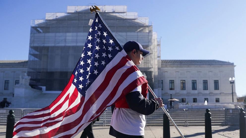 PHOTO: A person carrying a U.S. flag walks outside the U.S. Supreme Court as justices hear oral arguments on President Donald Trump's bid to preserve sweeping tariffs in Washington, November 5, 2025.