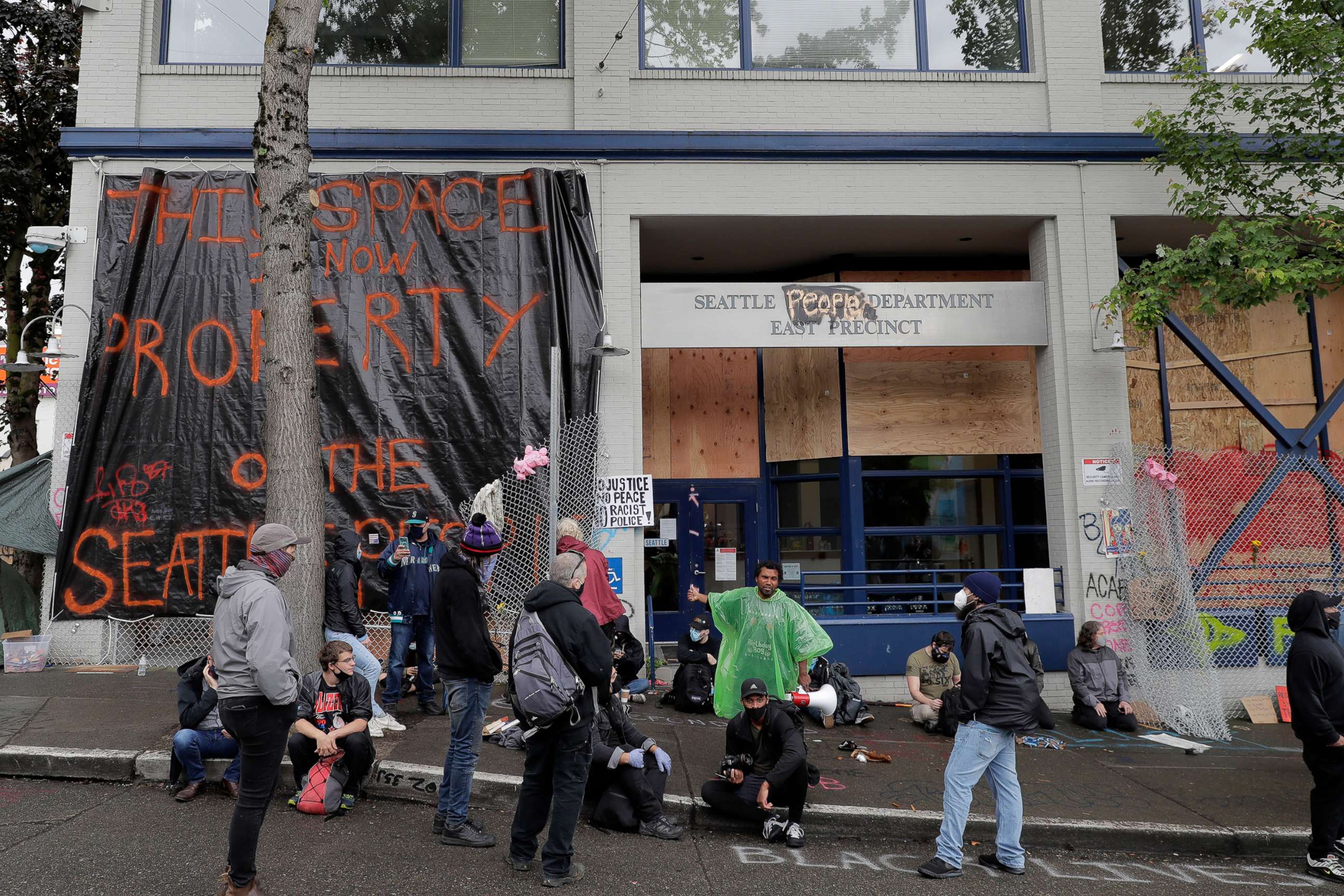 PHOTO: People sit in front of the Seattle Police Dept. East Precinct building, which has been boarded up and abandoned except for a few officers inside, June 11, 2020, in Seattle.