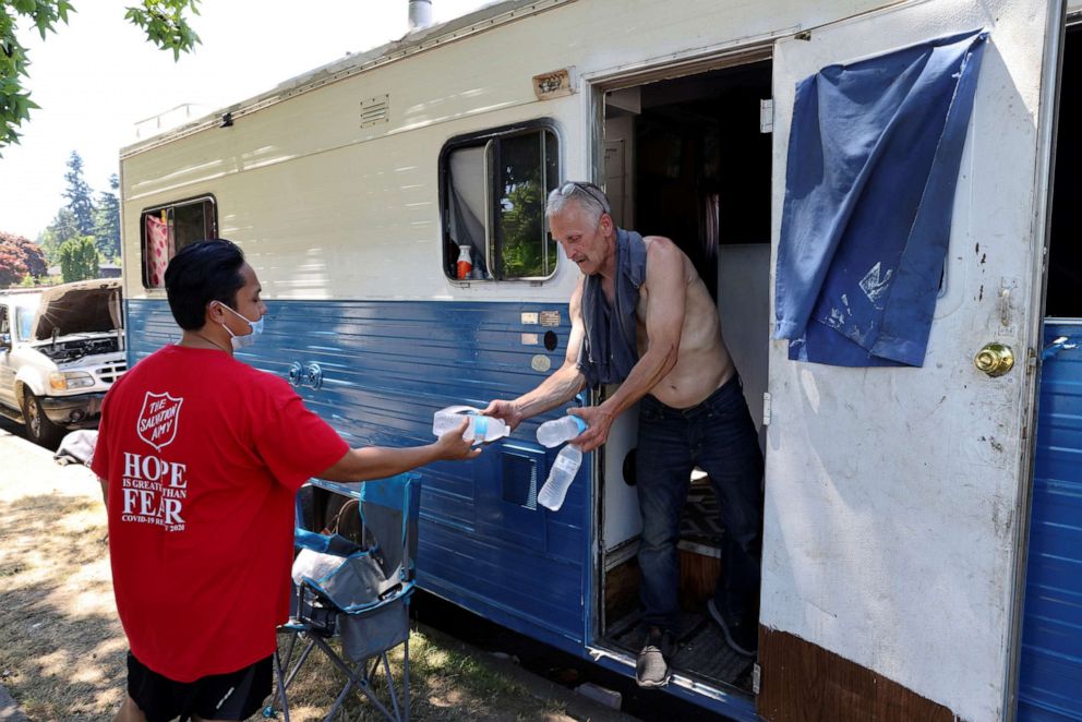 PHOTO: Shanton Alcaraz from the Salvation Army Northwest Division gives bottled water to Eddy Norby who lives in an RV and invites him to their nearby cooling center for food and beverages during a heat wave in Seattle, June 27, 2021.