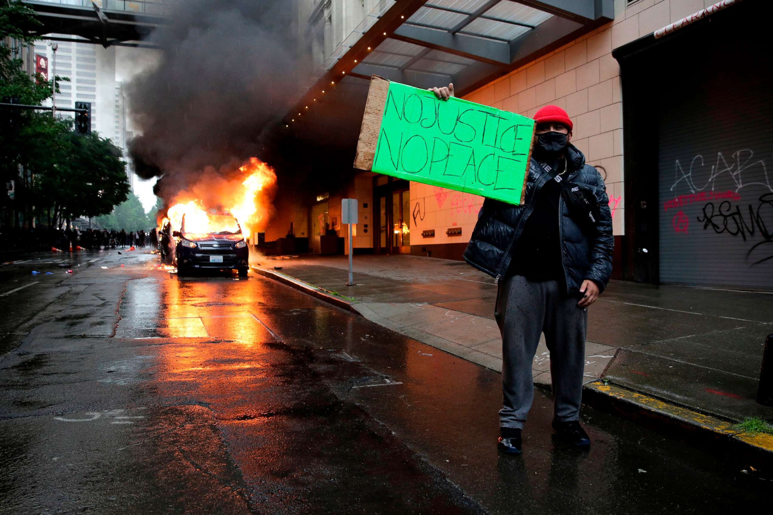 PHOTO: A man holds a sign in front of burning vehicles following demonstrations protesting the death of George Floyd, in Seattle, May 30, 2020.