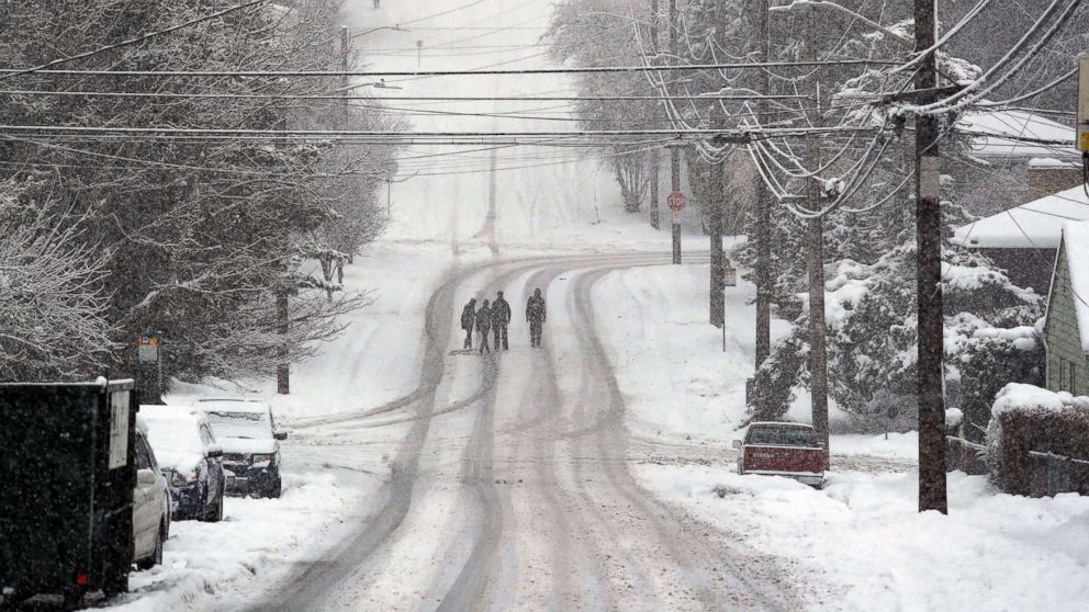 Pedestrians cross a deserted street as heavy snow falls, Feb. 11, 2019, in Seattle.