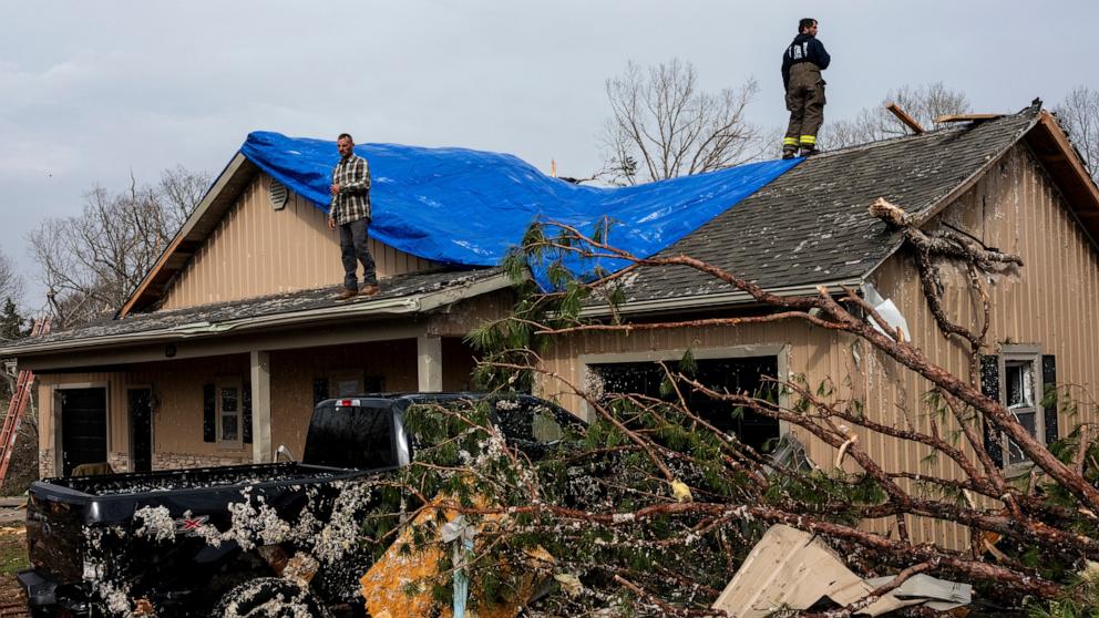 PHOTO: People help cover a roof damaged by a severe storm, March 15, 2025 in Poplar Bluff, Missouri. 
