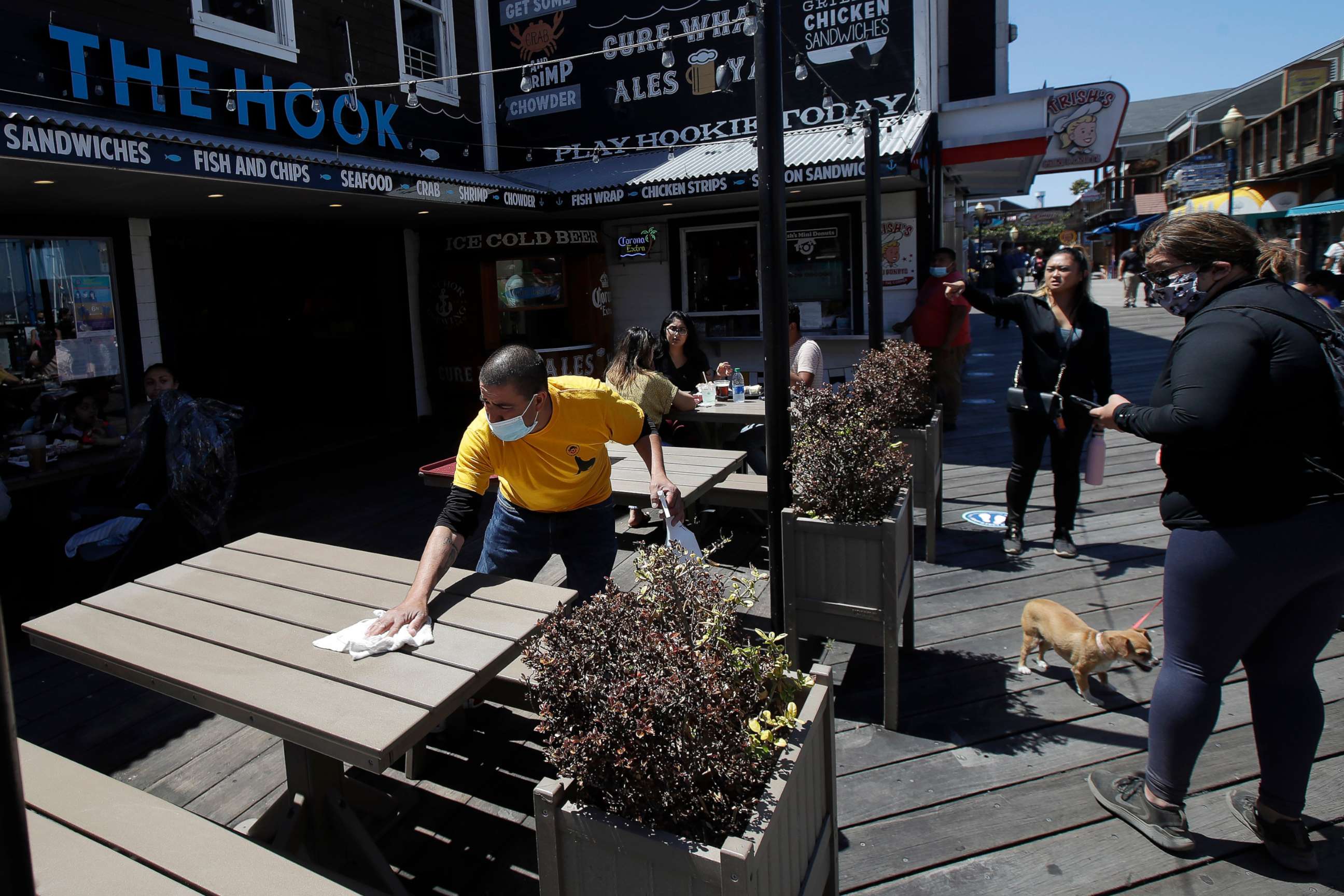 PHOTO: In this June 18, 2020, file photo a man wears a face mask while cleaning an outdoor dining table at The Hook at Pier 39, where some stores, restaurants and attractions have reopened, during the coronavirus outbreak in San Francisco.