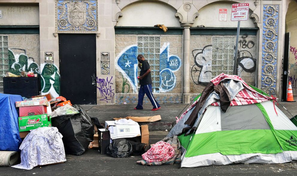 PHOTO: A man walks past tents housing the homeless on the streets  in the Skid Row community of Los Angeles, April 26, 2021.