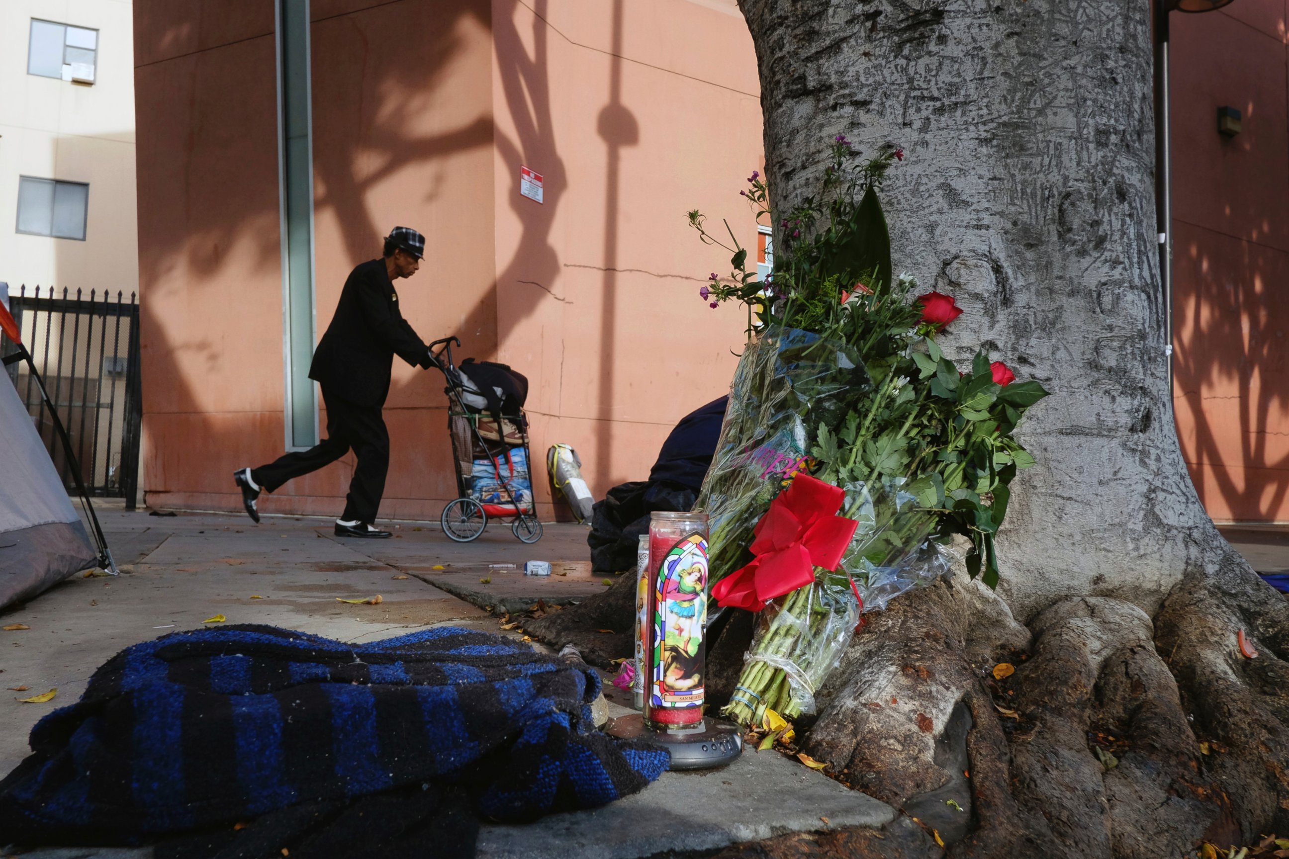In this March 2, 2015, file photo, a pedestrian walks past flowers and candles placed on a sidewalk near where Charly Keunang, a homeless man was shot and killed by police in the Skid Row section of downtown Los Angeles. 